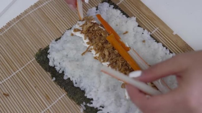 一个无法辨认的女人用手指将一块鱼糜放在她用来在厨房桌子上准备自制寿司的紫菜上的视频。