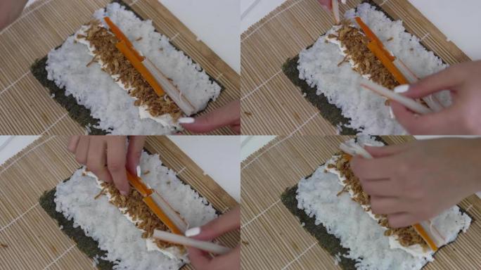 一个无法辨认的女人用手指将一块鱼糜放在她用来在厨房桌子上准备自制寿司的紫菜上的视频。