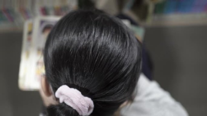 一个女孩正在图书馆看书。拍摄后视图。看过去。重点放在紫色发带上。重点放在紫色发带上。