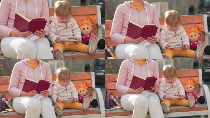 一个孩子坐在附近，用智能手机看动画片。女人正在坐在长凳上看书。幼稚的发展观