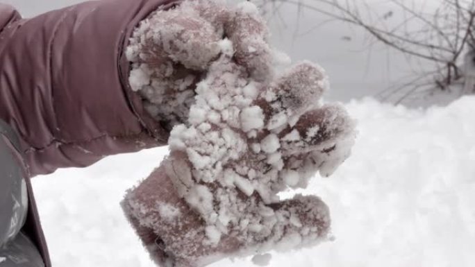 冬天，孩子戴着针织手套的手拿着第二只手套，上面覆盖着粘稠的雪块