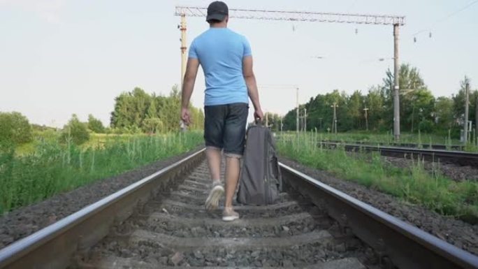 穿着帽子和短裤的男子沿着铁路铁轨行走，背着公路包
