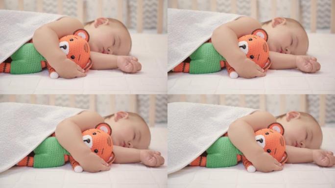 12-17个月大的幼儿睡在毯子下的床上，抱着一个针织老虎玩具。相机在滑块上从右向左移动，选择性对焦