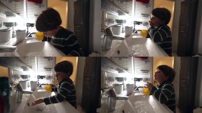 小男孩喝水，在浴室水槽里随地吐痰。孩子站在镜子前洗脸。睡前牙科常规