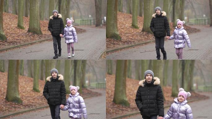 快乐的孩子男孩和女孩哥哥和姐姐走在秋天城市公园的小路上，落下的黄色叶子慢动作