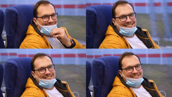 快乐的千禧一代男子坐火车，放下下巴上的医用口罩后对着镜头微笑。