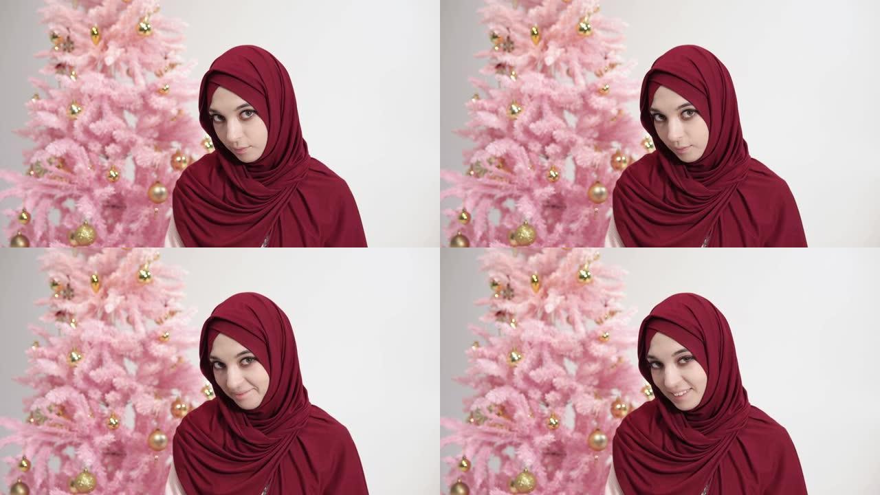 戴着头巾的穆斯林白人女士站在圣诞树背景上，看着相机