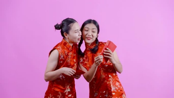 4K，肖像，两个穿着红色中国民族服装 (旗袍) 的亚洲女孩，其中两个在自己的红包中打开了钱，并震惊了