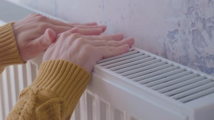 在寒冷的冬天，男人穿着黄色毛衣在家里的加热器上暖手
