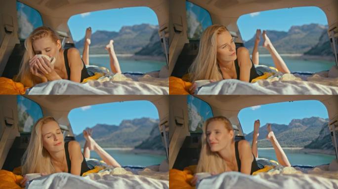 年轻女子，有着健康的金发，在湖边的一个大汽车后备箱里休息和露营。从杯子里喝茶