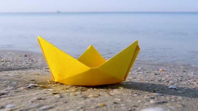 小纸黄船在海浪背景上靠近水面的沙子上特写。沙滩上的纸船夏天阳光明媚的日子。概念冒险旅行度假假期休息旅
