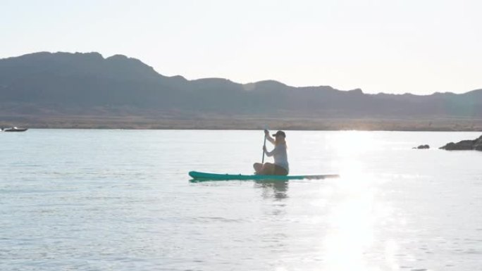 成熟的女人在平静的湖上划桨充气SUP