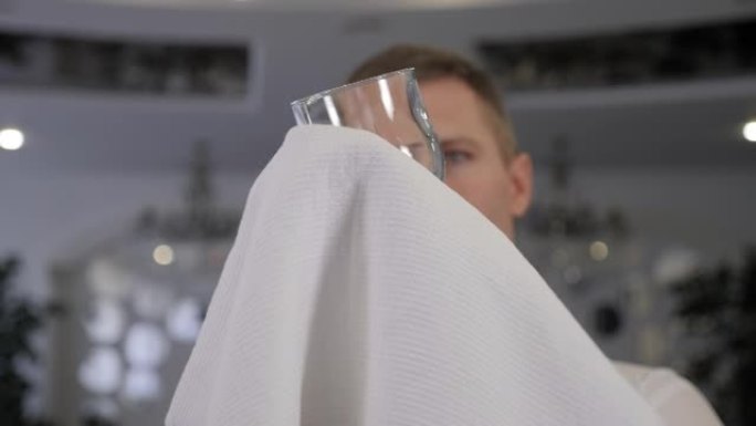 一个戴着白手套的服务员在餐厅用毛巾擦杯子。
