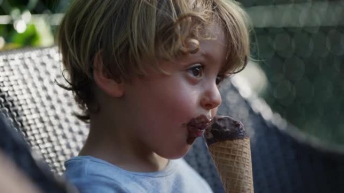 一个沉思的小男孩在外面吃巧克力冰淇淋蛋卷。沉思的孩子吃甜点