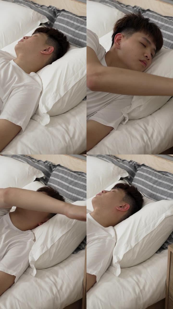 垂直屏幕: 亚洲年轻人按闹钟上的贪睡按钮，早上在家里的卧室里一直睡在床上。