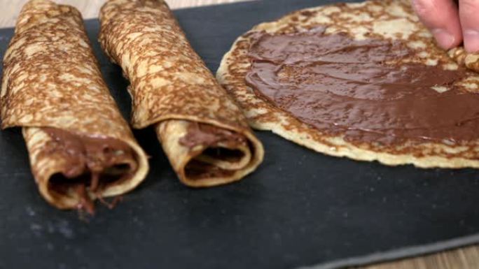 卷起薄饼，上面铺有榛子巧克力奶油，放在一块方形的黑色石板上，再加上两个现成的薄饼