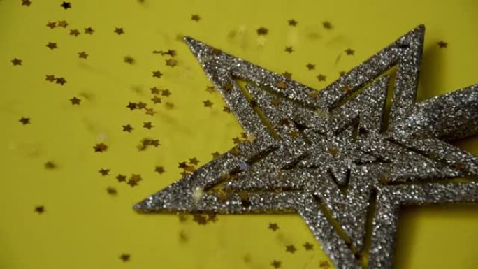 圣诞树上的玩具躺在黄色背景上，闪亮的金色星星落在上面。假期，圣诞节和新年概念
