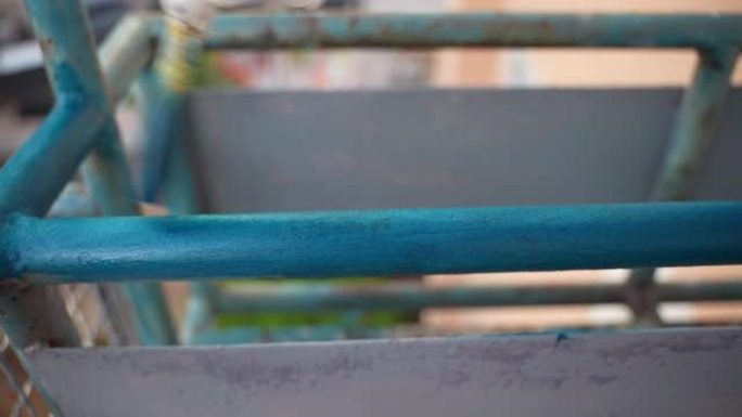 建筑工人手中的柔软画笔覆盖了蓝色的重建铁架，戴着手套的人在铁锈和腐蚀的金属表面上漆。油漆外部金属结构