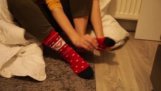穿着红色图案袜子的女人坐在寒冷房间的地板上，光线昏暗。用白色保暖毯包起来，穿上袜子。室内低温。没有暖