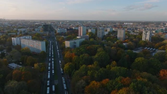 向前飞行在秋季公园的宽阔道路上停放的一排排公共汽车上。蒂尔加滕和周围的住宅区在日落时分。德国柏林