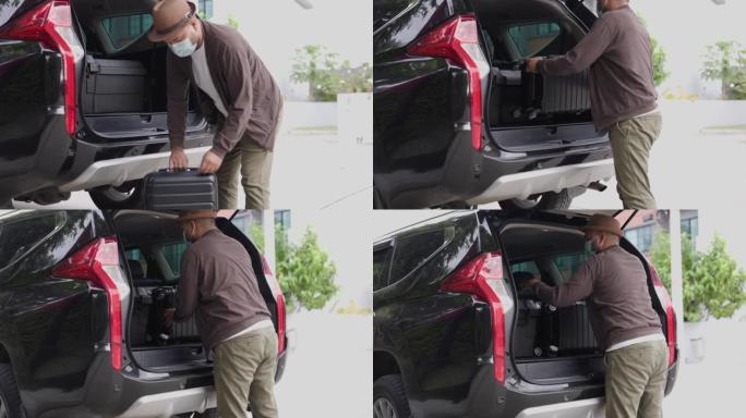 一个年轻人把他的手提箱放在汽车后面，准备离开。打开汽车后部放行李到其他省份旅行。戴口罩保护冠状病毒。