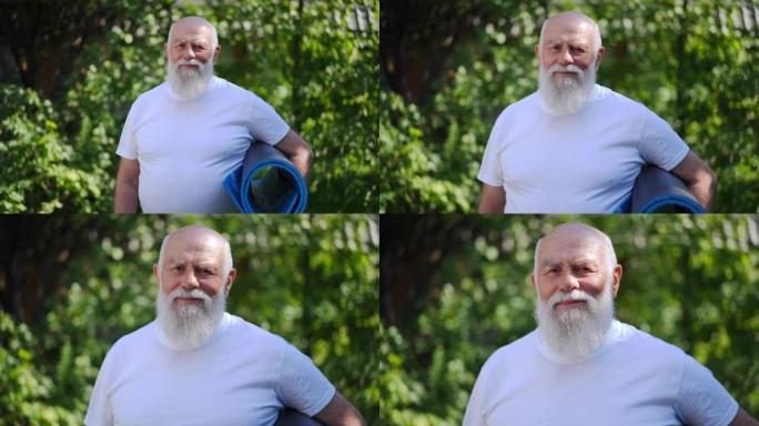 现场摄像机接近微笑的大胡子男子在户外与运动垫合影。放大公园阳光明媚的夏日里积极自信的高加索老退休人员