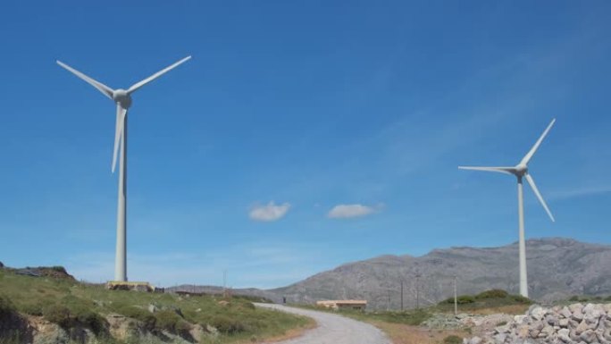 晴天，两个风力涡轮机和道路在山丘景观之间