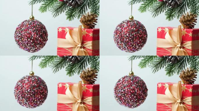 一个闪亮的粉色球在一棵白雪覆盖的圣诞树上旋转，一份带有丝带的红色礼物。