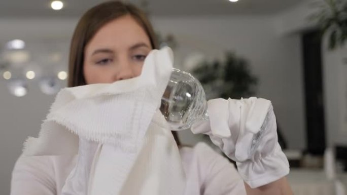 一个年轻的女服务员在一家餐馆用白色餐巾纸擦杯子。