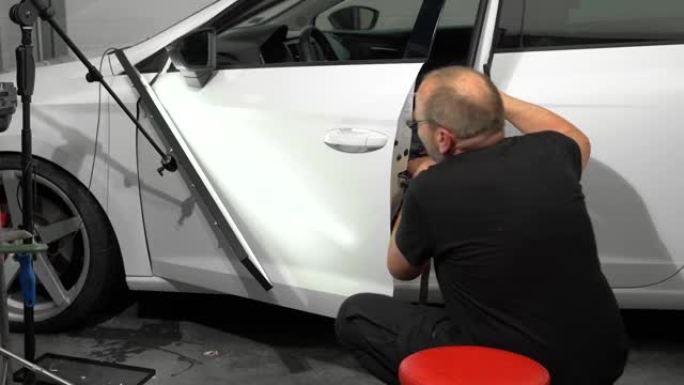汽车修理厂维修左车门表面凹痕的过程。技术人员正在使用工具进行无油漆凹痕修复。