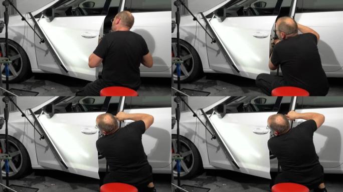 汽车修理厂维修左车门表面凹痕的过程。技术人员正在使用工具进行无油漆凹痕修复。