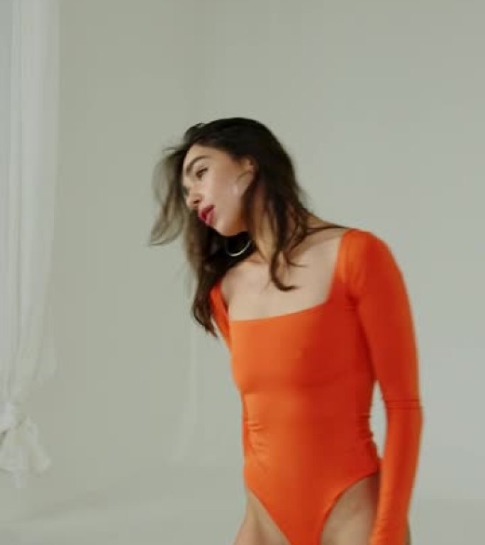 穿着橙色泳衣的运动制服的美丽模特女孩摆姿势，并将头发固定在白色背景上。垂直视频