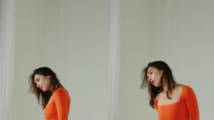 穿着橙色泳衣的运动制服的美丽模特女孩摆姿势，并将头发固定在白色背景上。垂直视频