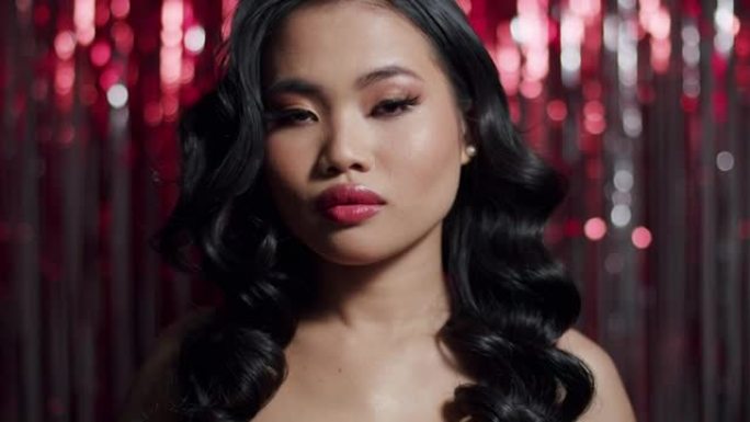 迷人魅力的亚洲女性，性感的外表在红色闪亮的背景下对着相机摆姿势。