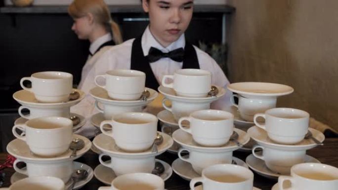 女服务员在现代餐厅为工作日准备茶杯套装。