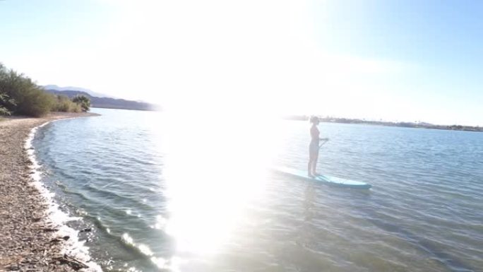 年轻的女飞行员在宁静的湖上站起来划桨板 (SUP)