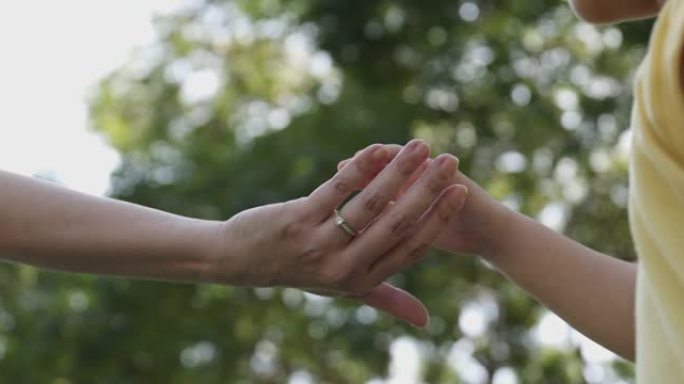 4k视频慢动作妈妈和女儿手牵手，绿色公园背景。