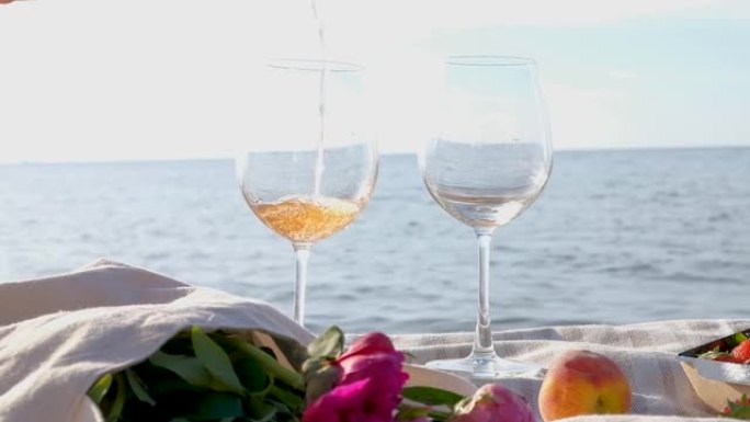 用手将玫瑰酒倒入玻璃杯中，背景是平静的大海。夏季野餐