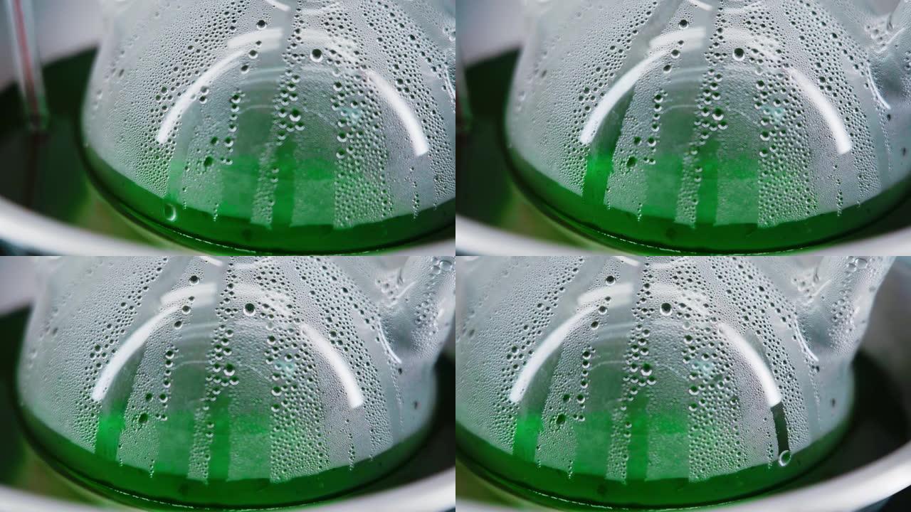 带有绿色液体的雾状玻璃烧瓶。特写。水滴从烧瓶中流出。化学反应。食用色素生产。实验室。水平全景。摄像机