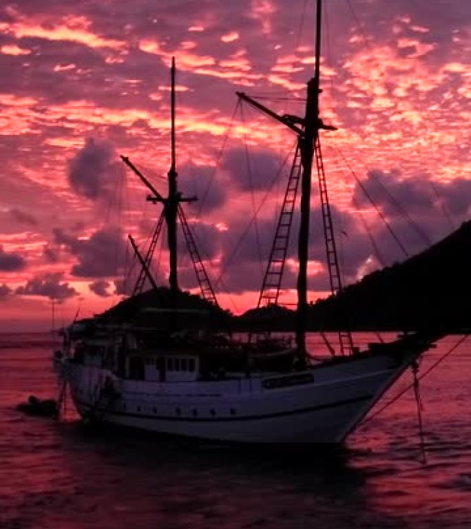 沿热带岛屿停泊的船上彩色日落的空中拍摄的垂直视频