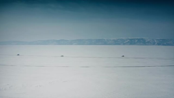 在晴朗的蓝天和山脉的背景下，三辆探险车辆在贝加尔湖白雪覆盖的荒原中间行驶。俄罗斯西伯利亚贝加尔湖。无