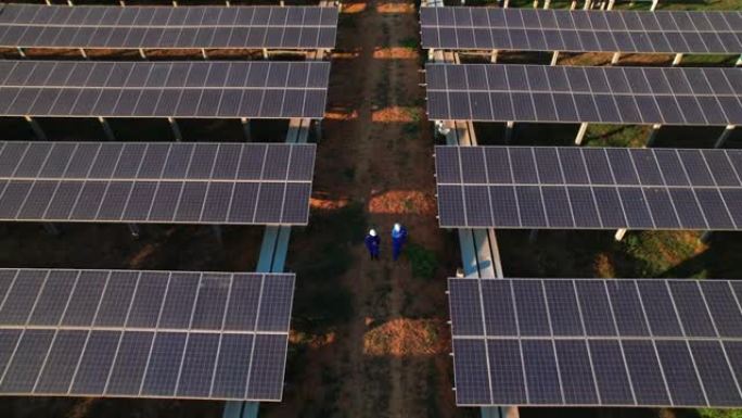 在农村养鱼场附近的太阳能电池板农场之间的小线上行走的男女蓝领工人的鸟瞰图