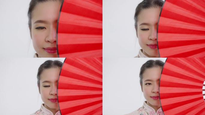 中国/亚洲美女脸部特写旗袍白色碎花图案连衣裙在中国新年节日，红色的扇子遮住了她的左半张脸，看着镜头
