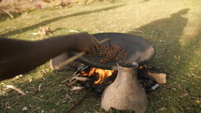 在埃塞俄比亚，一名妇女在户外大火的锅中煮咖啡豆