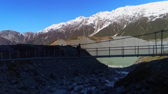 徒步旅行者沿着悬索桥漫步，冲向急流的河水，到达雪山