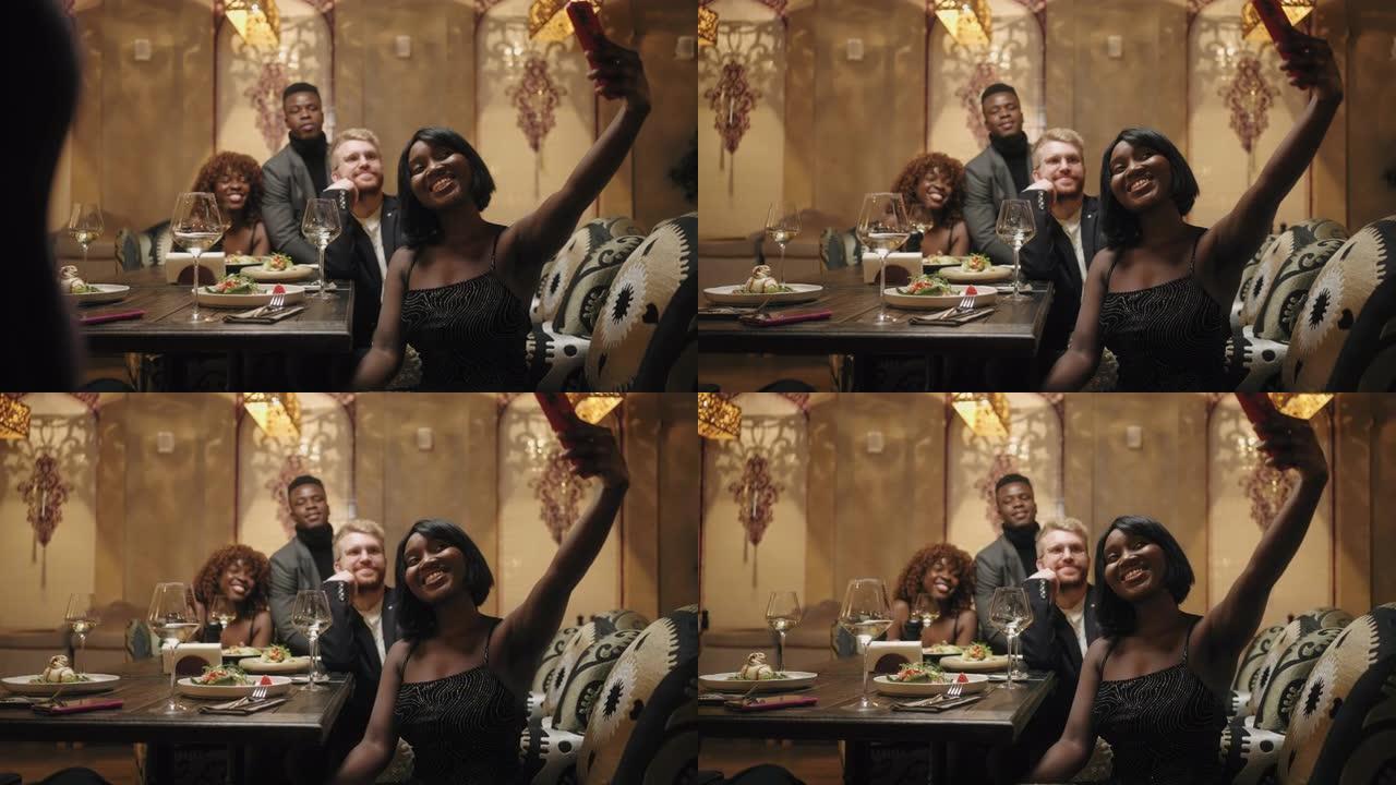 黑人妇女和她的多民族朋友在餐厅用智能手机自拍，快乐的人