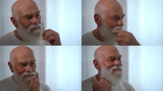 大胡子白种人梳理头发微笑的镜子里的特写反射。白发和棕色眼睛的老男性退休人员早上在浴室里准备。慢动作。