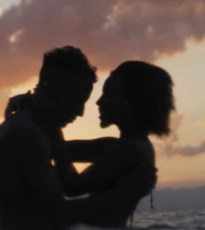 非洲民族浪漫的异性恋夫妇在日落时一起在海里游泳。互相拥抱垂直视频