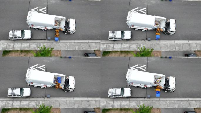 废物设施卡车伸出机械臂并装载一箱可回收物的俯视图。