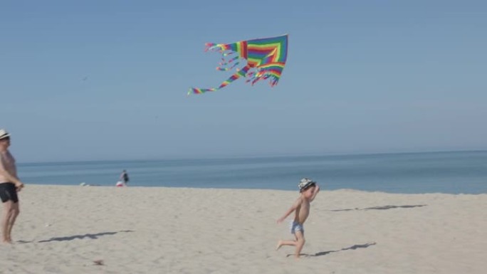 父子俩在天空中奔跑沙滩飞舞彩虹风筝。小男孩跑沙试图在空中放风筝。